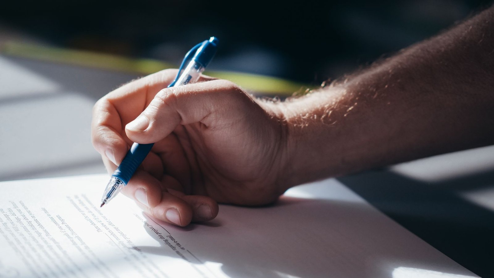 Mano con un bolígrafo azul firmando un documento, como quien acepta los términos comerciales de Meta